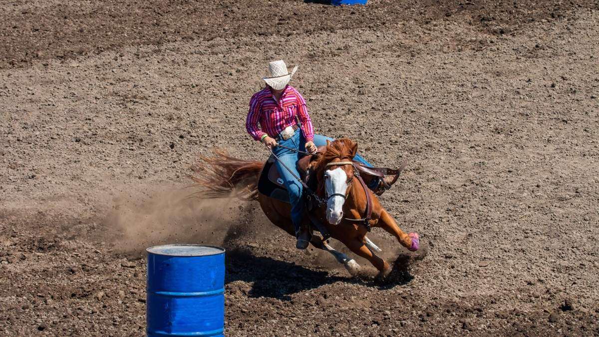 Barrel racer turning a blue barrel in a dirt arena