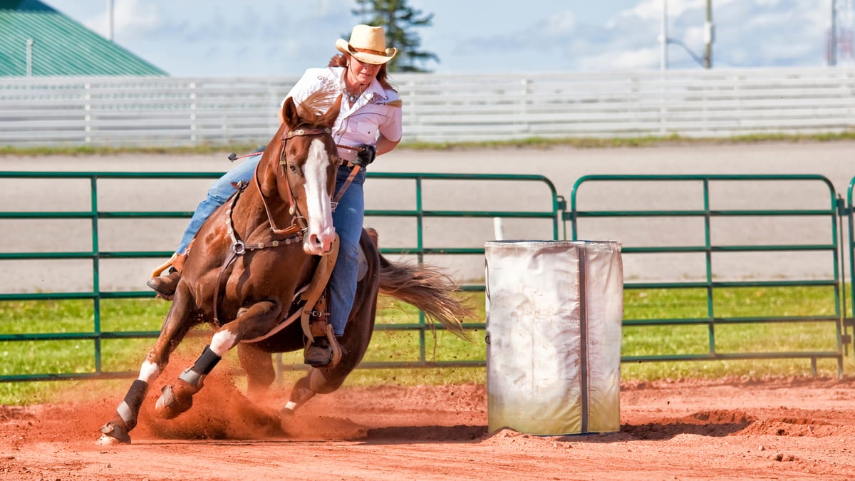 Cowgirl and bay horse turning tightly around a barrel in a dirt arena